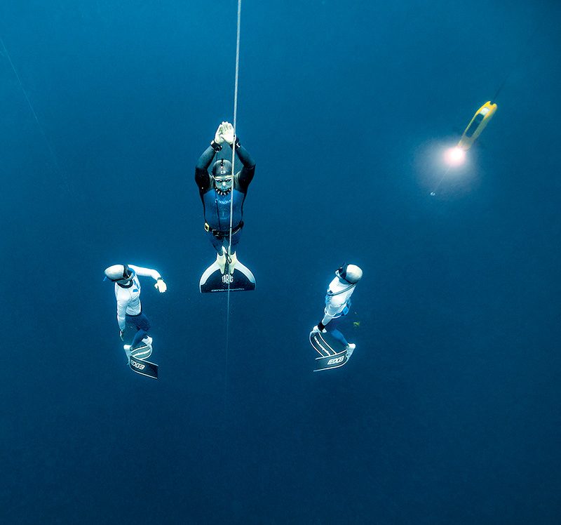 free diver ascending flanked by two safety divers