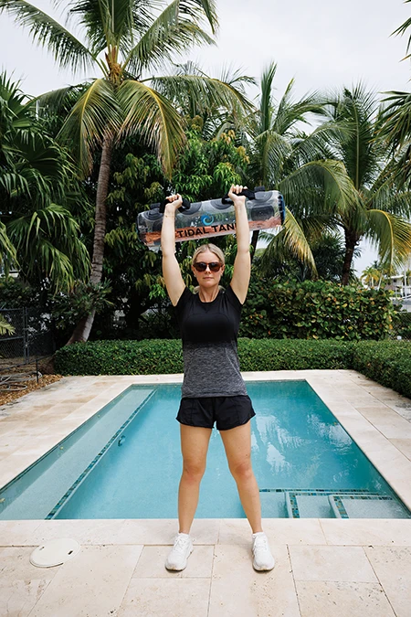 Woman extends legs while pressing arms to hold the bag above her head.