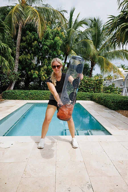Woman stands with left hand in front of her and grabs the bag or handle on its left side. She swings the bag in front of her.