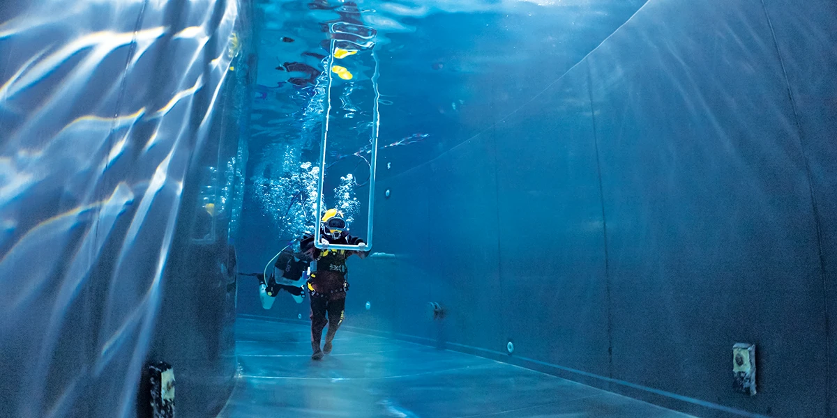 A diver wearing a heavy drysuit, dive helmet, and chemical-resistant gloves.
