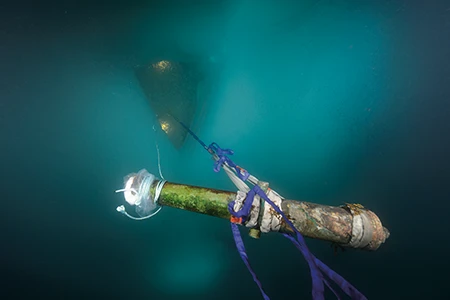 A cannon is hoisted toward the surface during an early on-ice artifact recovery operation in the Arctic.