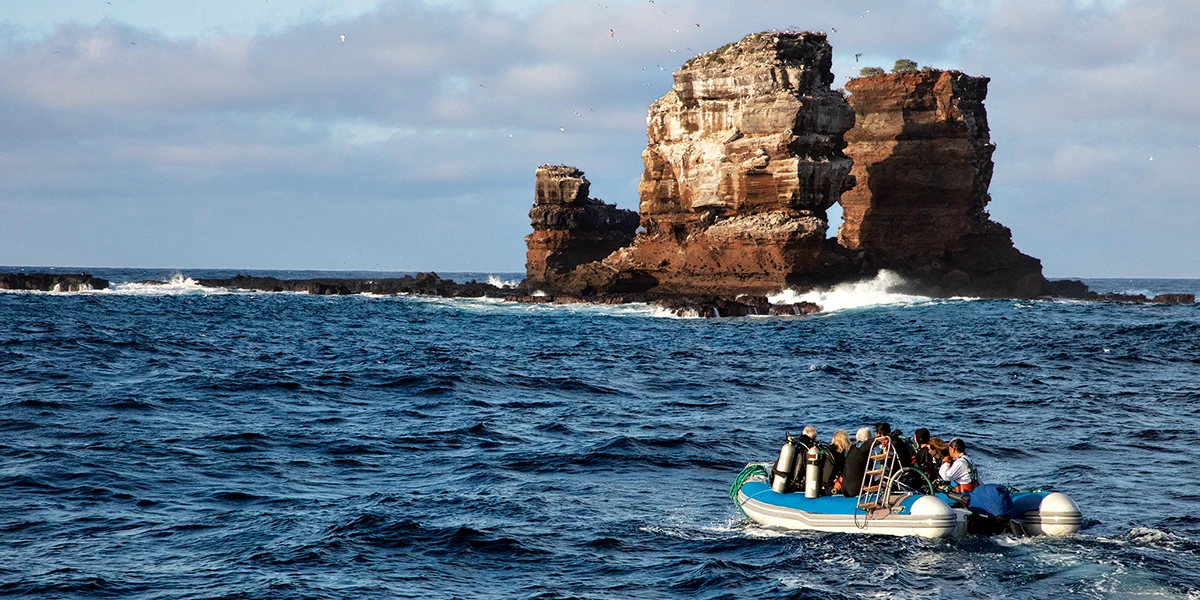 A boat in the ocean moves across the water toward a cliff.