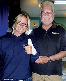 Woman with a bandged left hand stands next to a bespectacled, bearded man